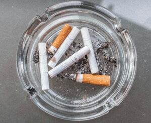 Glass ashtray containing several cigarette butts and scattered ash